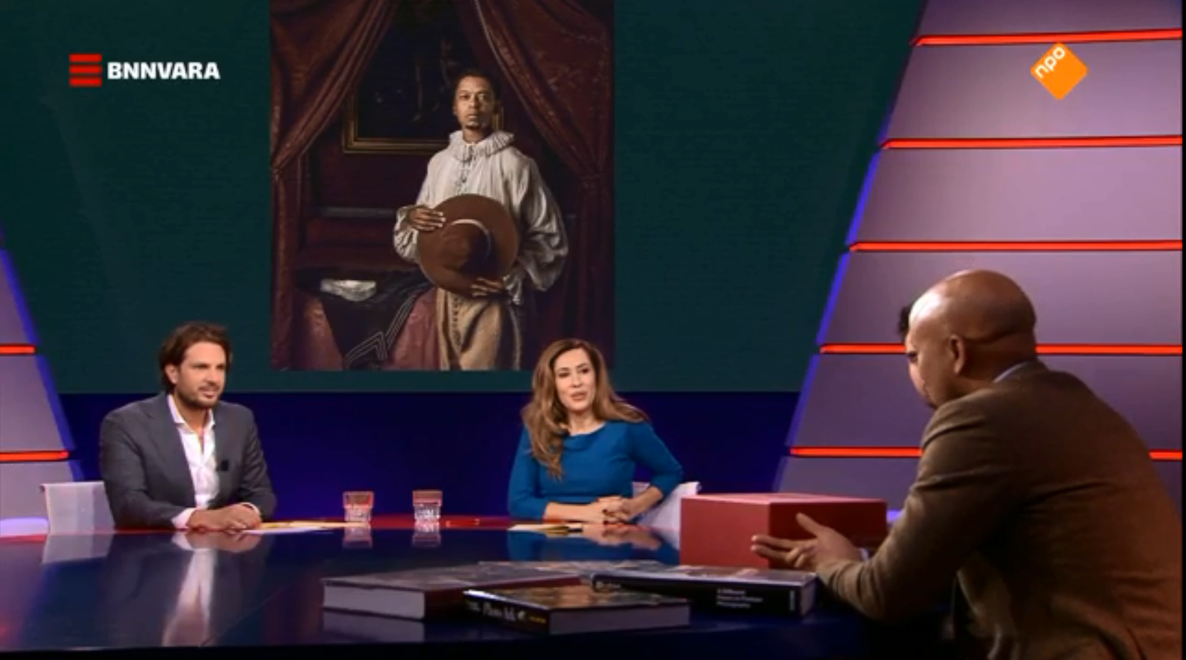 Humberto Tan aan tafel bij De Vooravond met in achtergrond de foto die hij nam voor de tentoonstelling Hollandse Meesters Her-Zien welke afgedrukt is in The New York Times